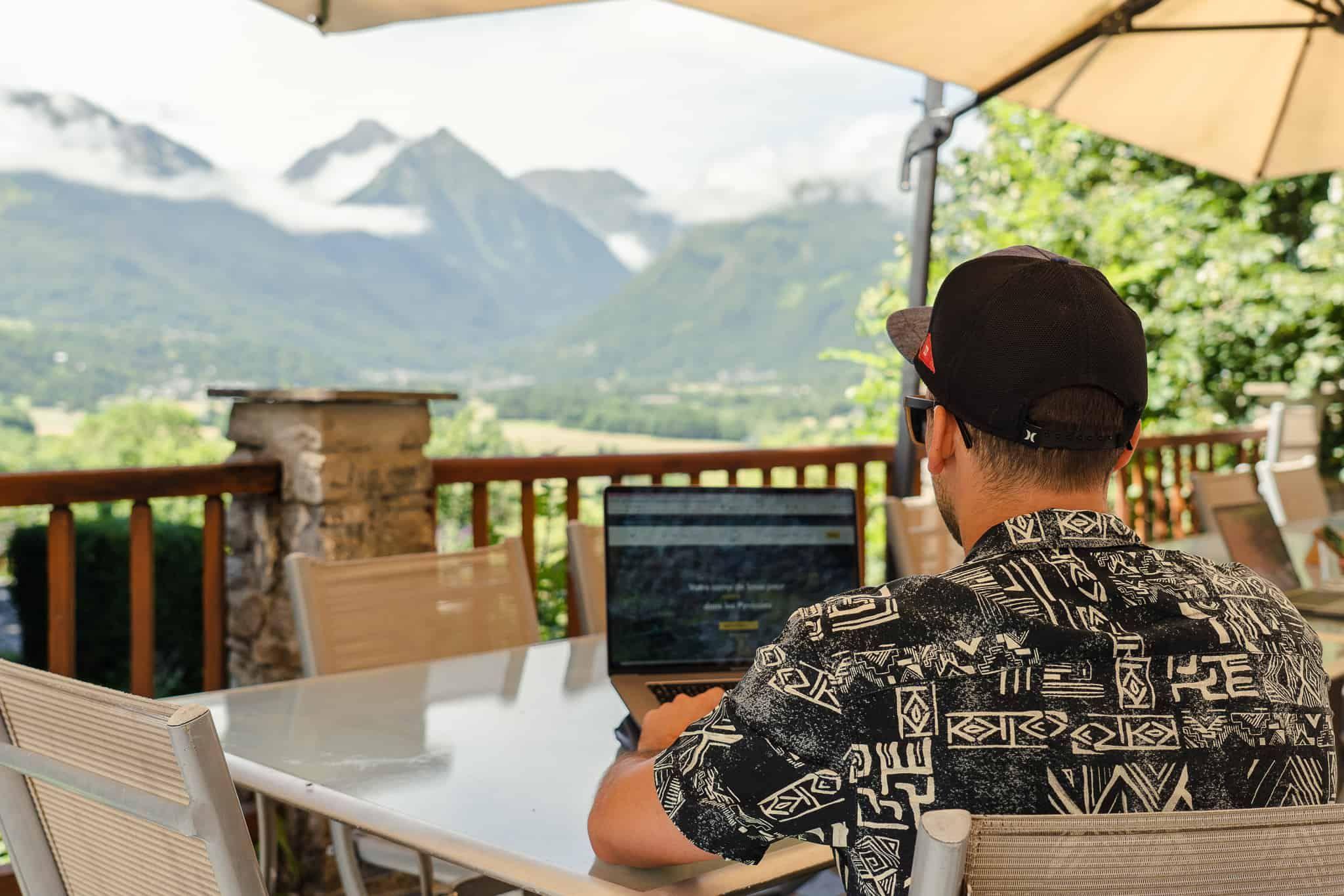 Person working on a laptop on the outdoor terrace with breathtaking Pyrenees mountain views