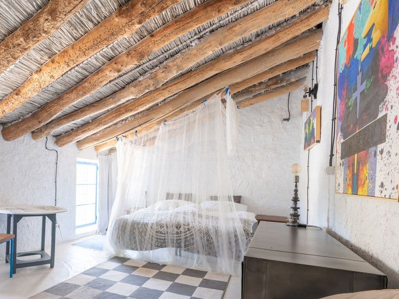 Private double room with a canopy bed, exposed wooden beam ceiling, checkered tile floor, and colorful artwork on the wall
