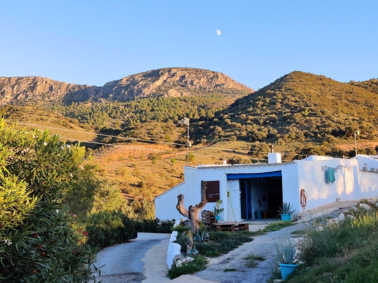 Exterior view of the REC.ON residence building at sunset with mountains behind and the moon visible in the sky