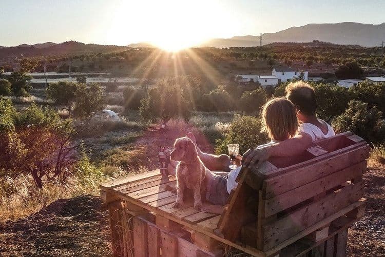 Couple sitting on a pallet bench with their dog watching the sunset over the Andalusian village and mountains