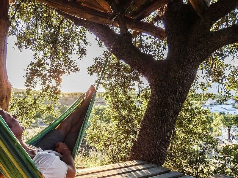 Person lying in a hammock on the tree platform, surrounded by lush tree canopy with village views below