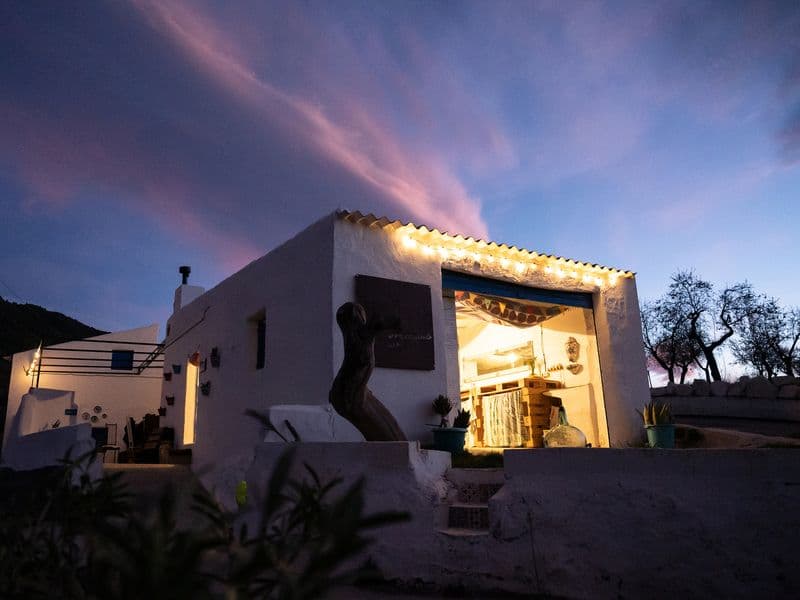 Exterior view of the REC.ON Gallery building at dusk, lit up with fairy lights, with a sculpture in front