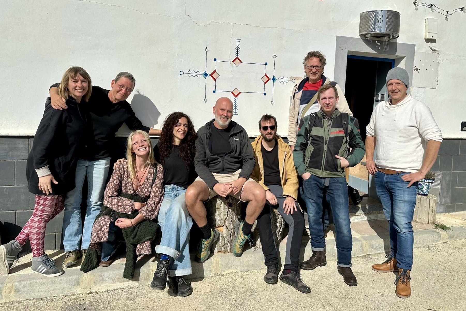 Group of nine people posing together in front of a white building with a decorative mural