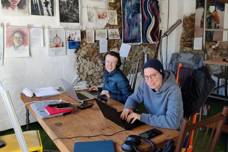 Two people working on laptops at a wooden table inside the gallery coworking space, surrounded by artwork on the walls
