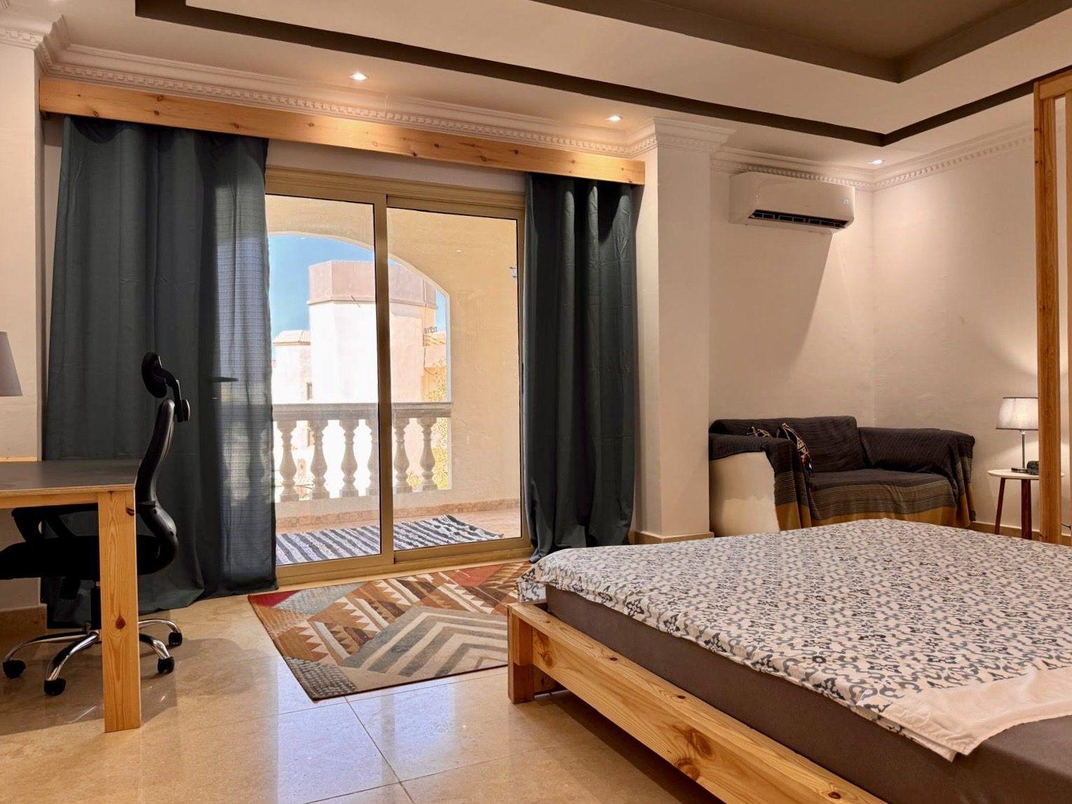 Spacious double room with wooden bed, work desk with ergonomic chair, air conditioning, and sliding doors leading to a balcony