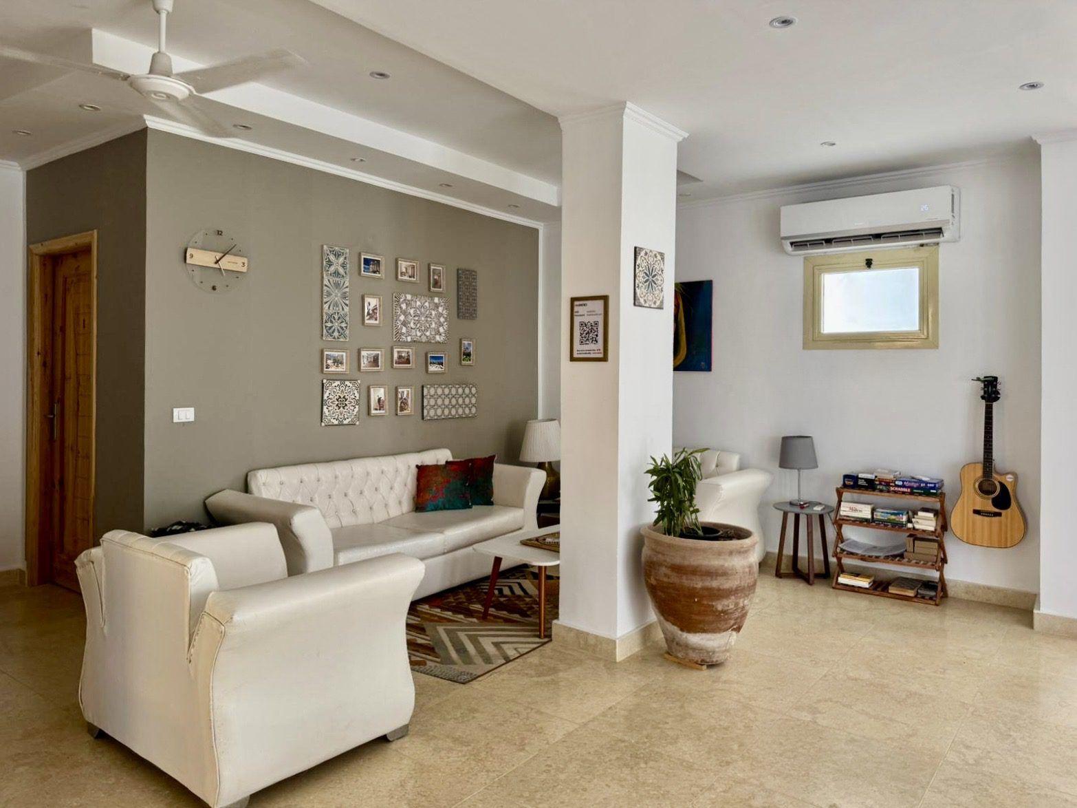 Spacious indoor lounge with white sofas, photo wall, guitar, and air conditioning