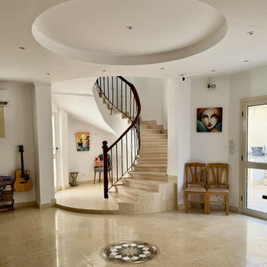 Grand entrance hall of the villa featuring a spiral staircase with marble steps and iron railings, artwork on walls