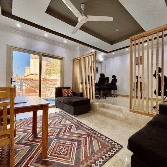Indoor coworking space with wooden slatted dividers, ergonomic office chairs, sofas, and view to the pool area