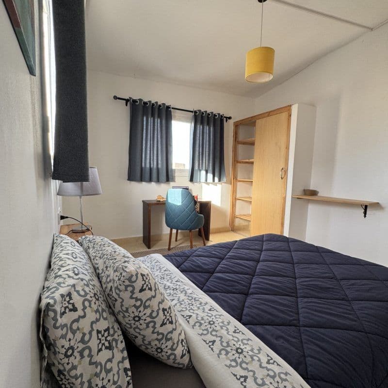Double room with bed, work desk, blue chair, wooden wardrobe shelving, and pendant lamp