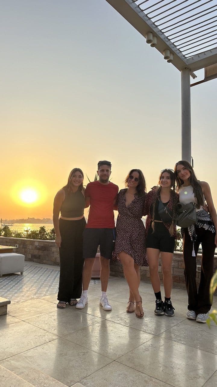 Group of five community members posing together on a terrace at sunset with sea views