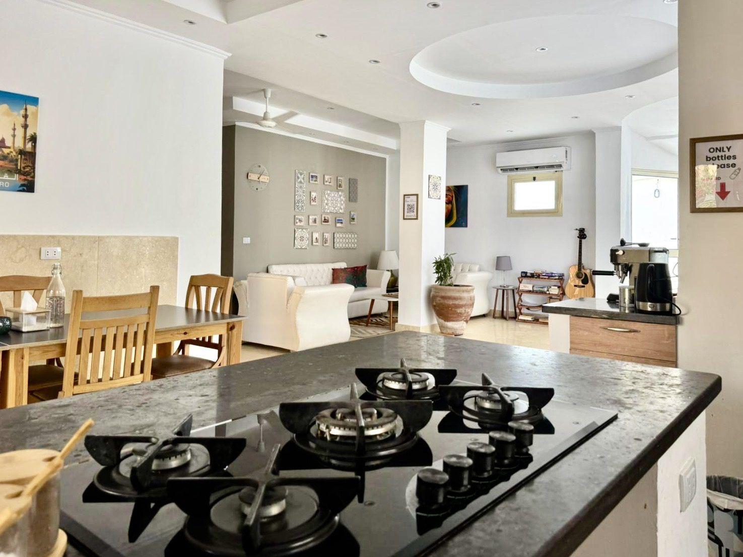 View of the community kitchen with gas hob in the foreground and the lounge area with sofas and staircase in the background