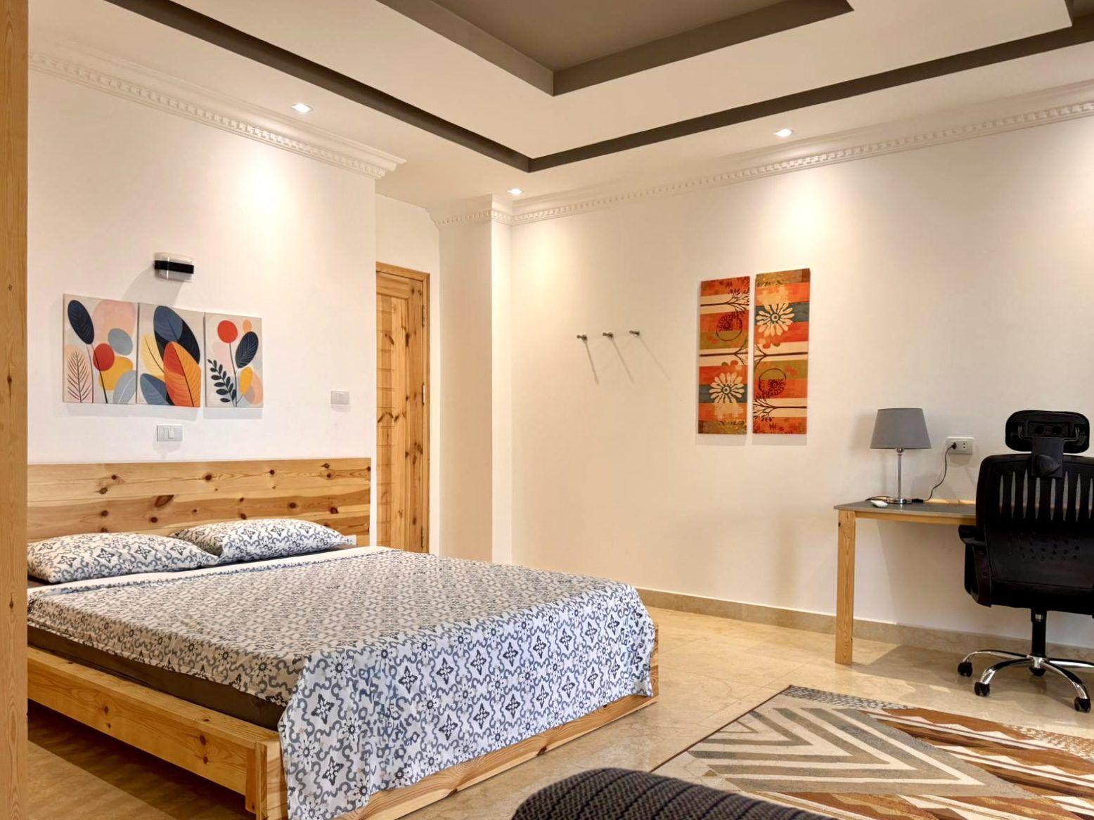 Spacious double room with wooden bed, ergonomic desk chair, and artwork on the walls