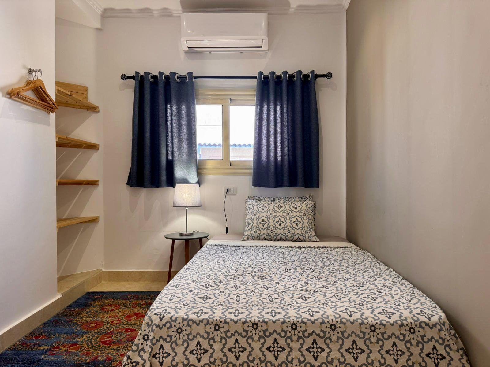 Single room with single bed, wardrobe shelves, lamp, and air conditioning