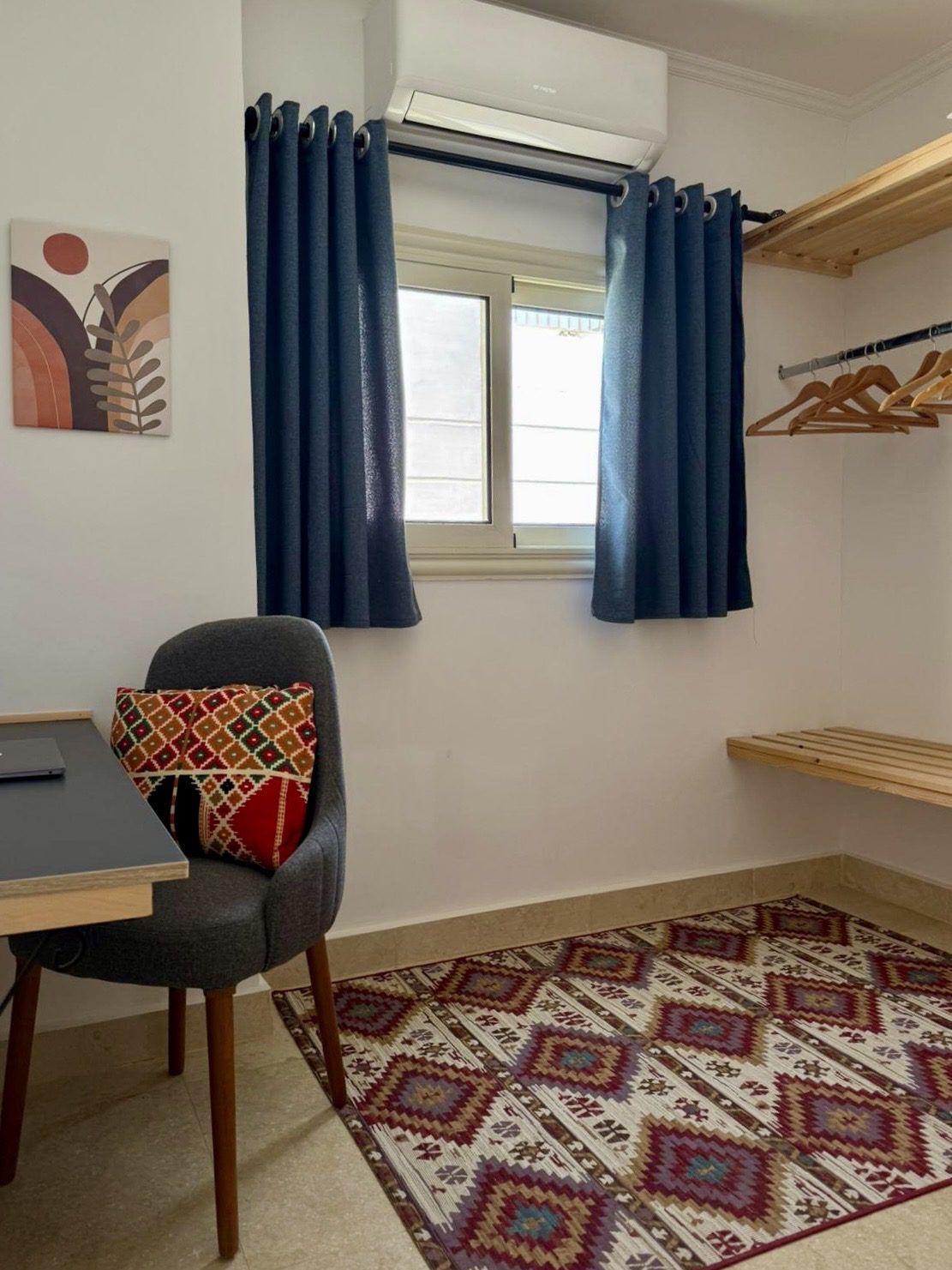 Small private room with work desk, chair, wardrobe shelves, and air conditioning