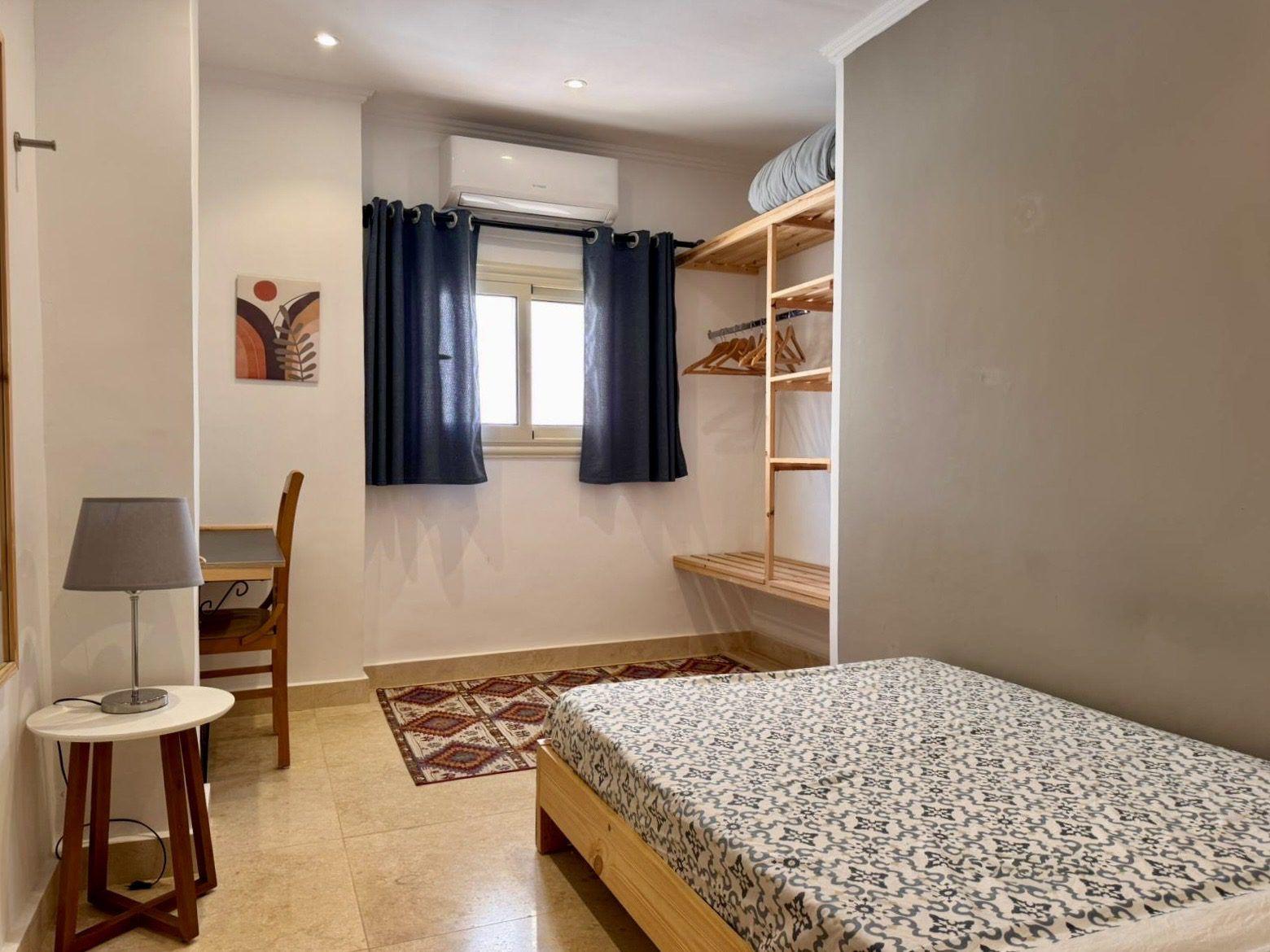 Single room with bed, desk, lamp, wardrobe shelves, and air conditioning