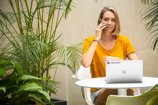 Woman working on laptop outdoors in a plant-filled courtyard, repeople branded laptop