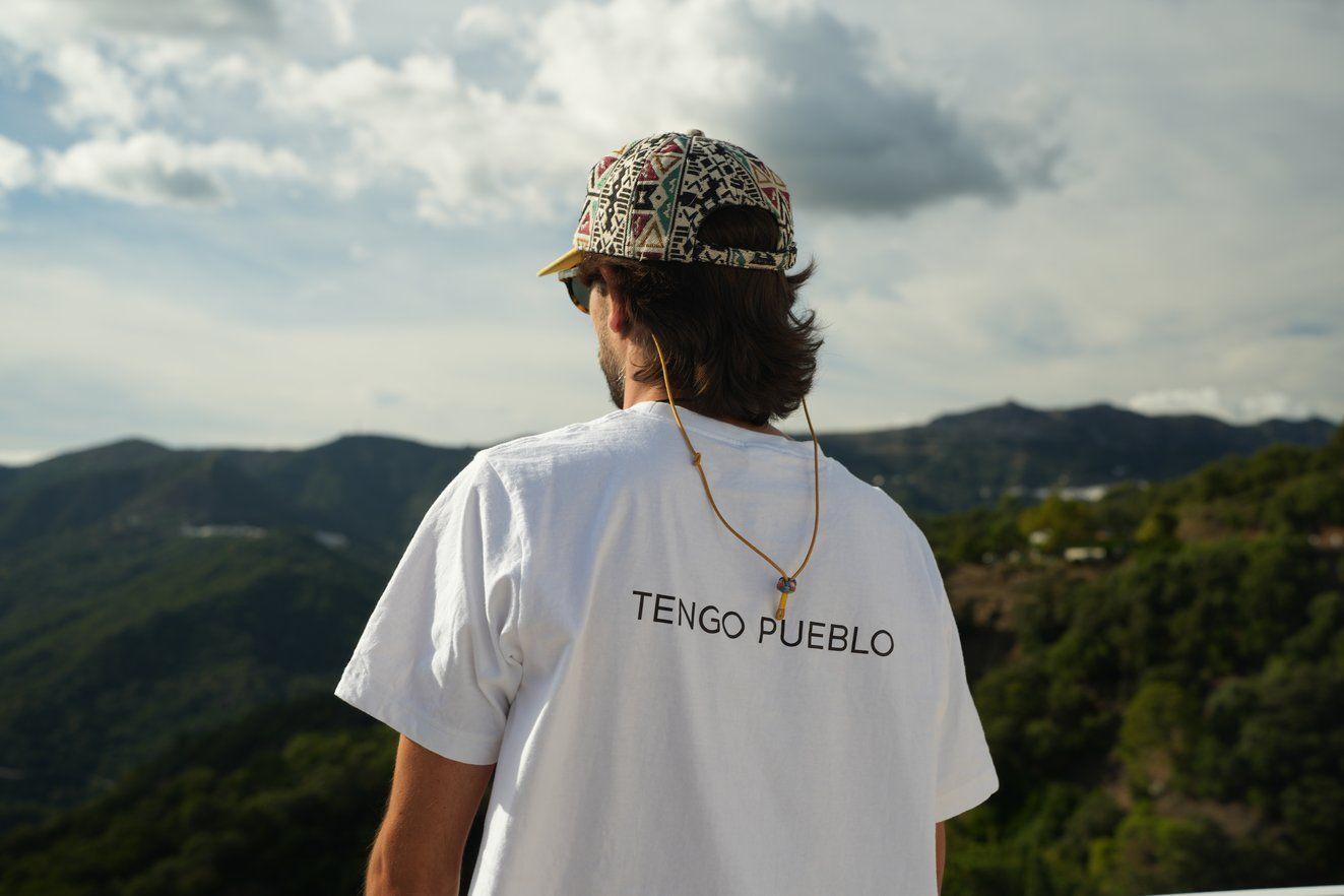 Person wearing a 'Tengo Pueblo' t-shirt looking out over the green mountain landscape of Benarrabá