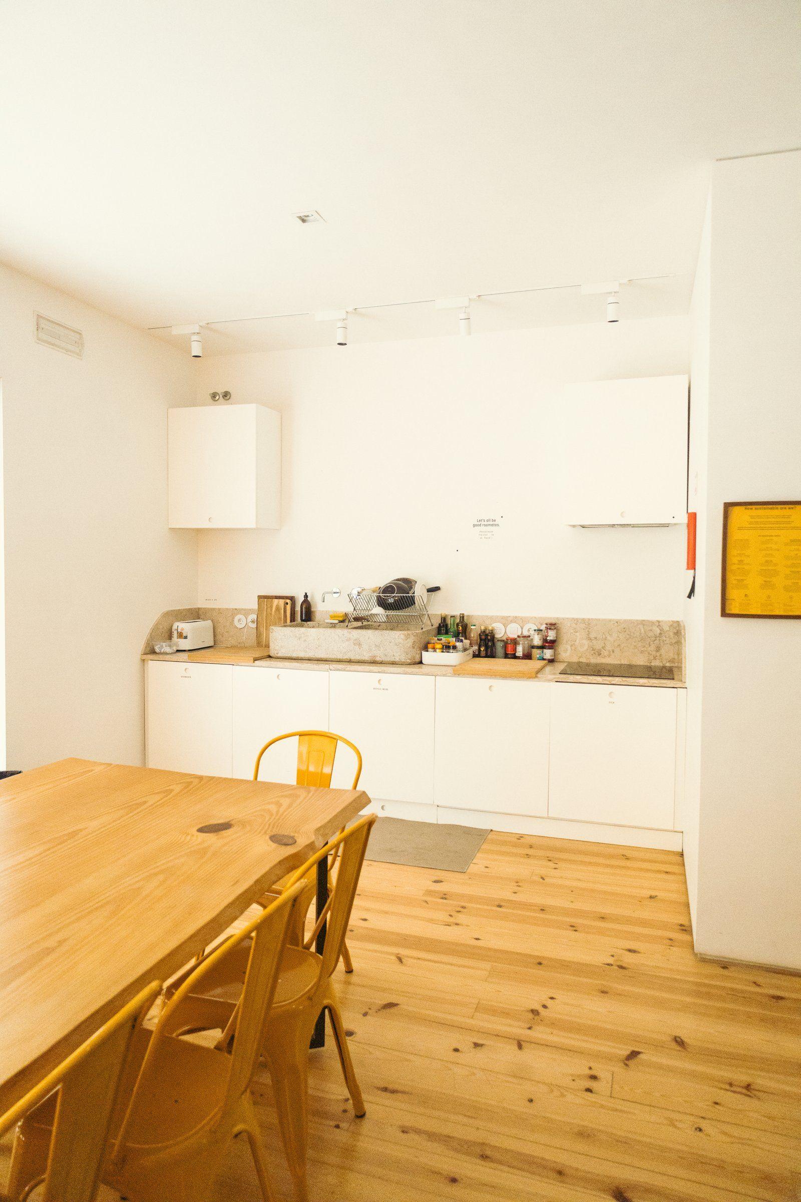 Shared kitchen with white cabinets, stone countertop, wooden dining table and yellow metal chairs