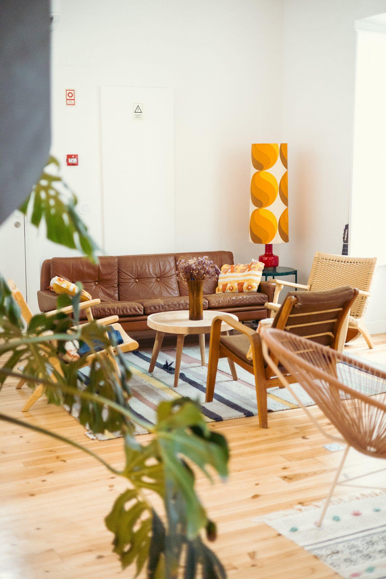 Shared lounge area with retro 60s design — brown leather sofa, wooden chairs, round coffee table, plants and a yellow lamp