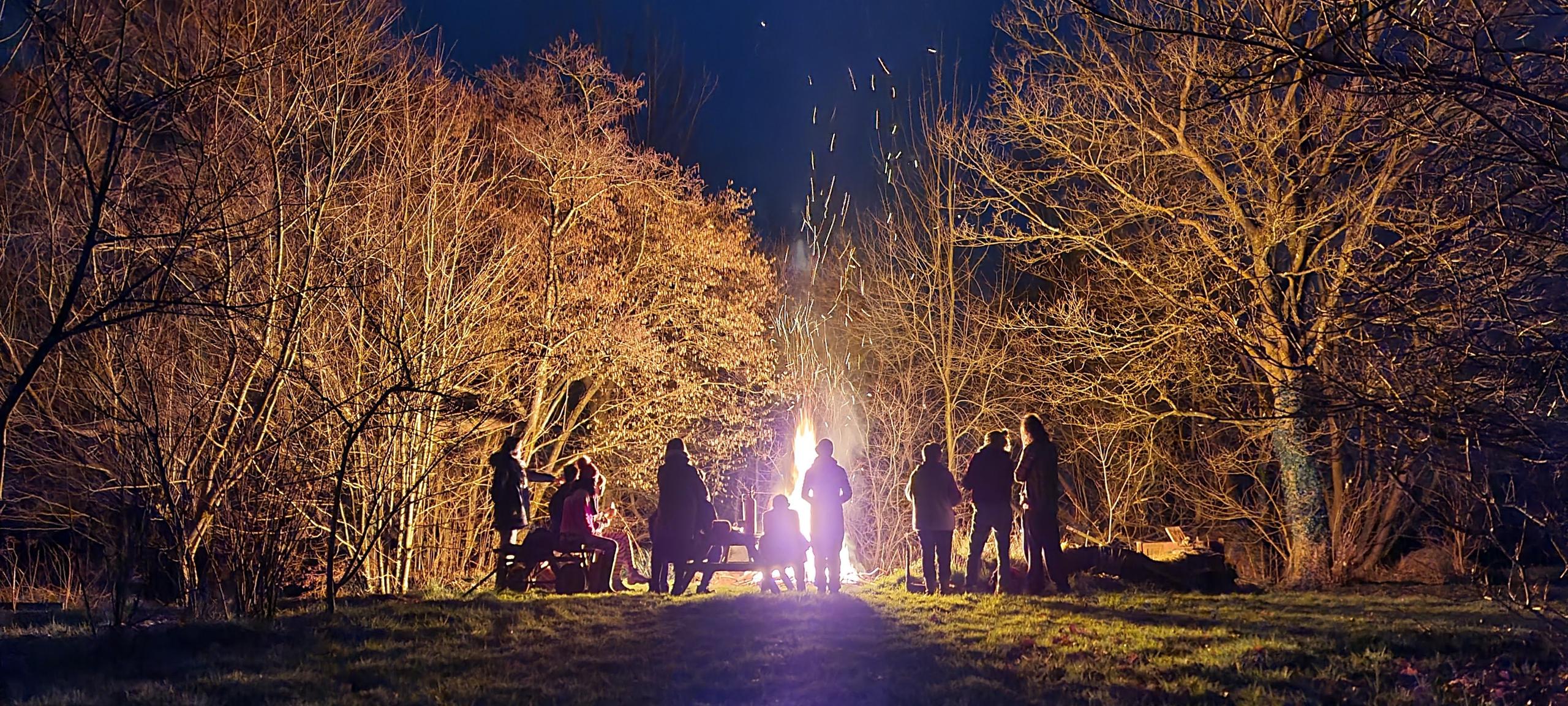 Group of colivers gathered around a bonfire at night in the outdoor grounds