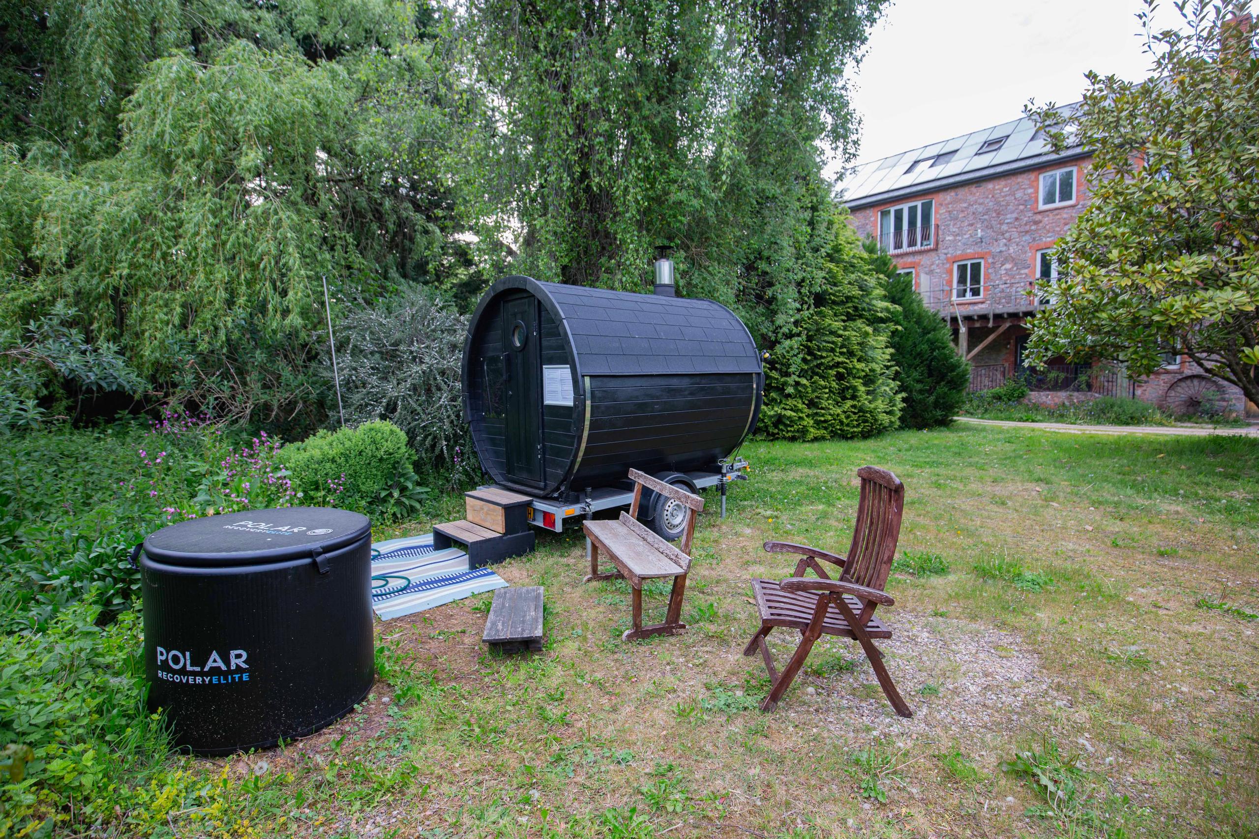 Outdoor sauna barrel and Polar cold dip tub in the garden with the Mill House in the background