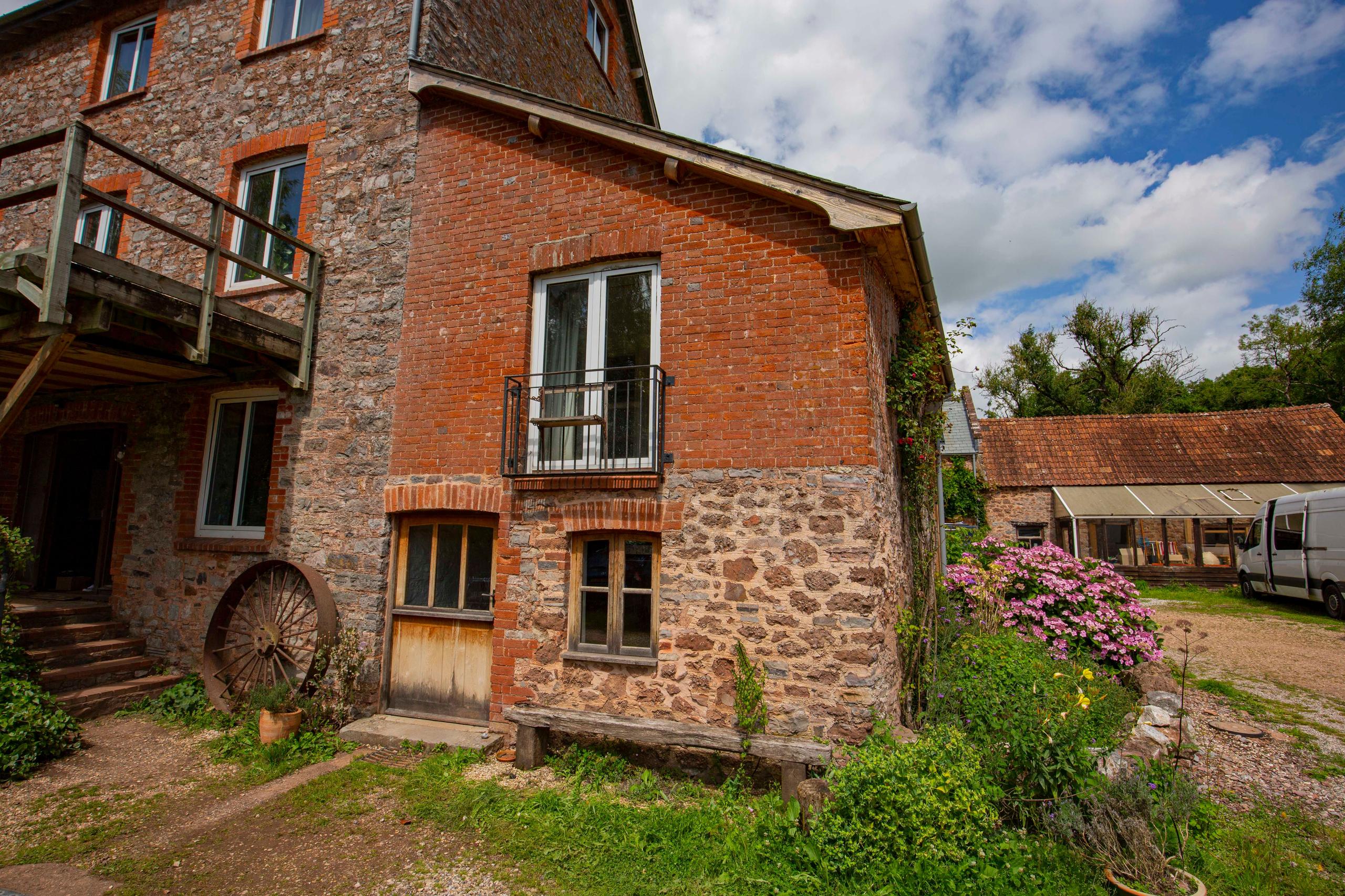 Exterior view of the Annex Apartment cottage with brick and stone facade, balcony and garden