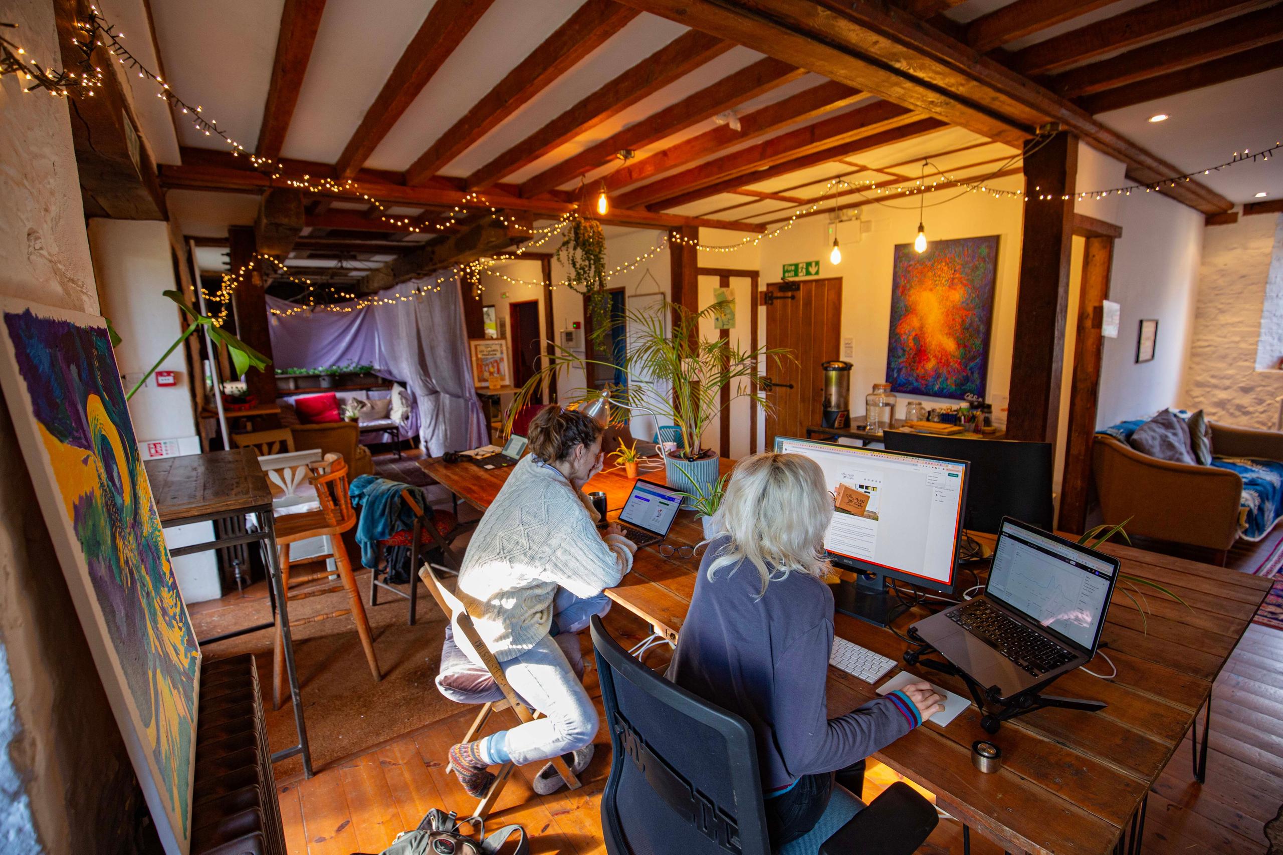 Two colivers working on laptops at desks in the coworking space with fairy lights and artwork on the walls