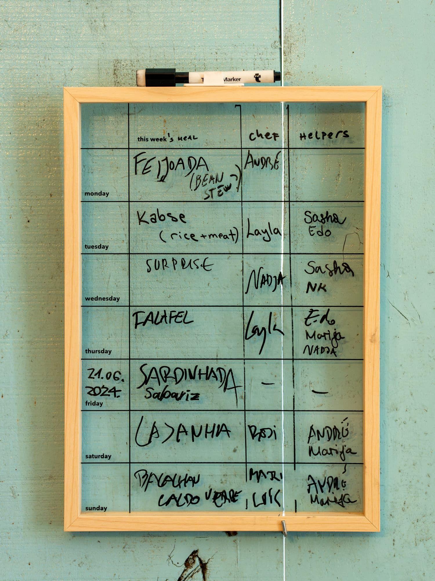 Weekly dinner cooking calendar whiteboard showing meal schedule with chef and helper assignments