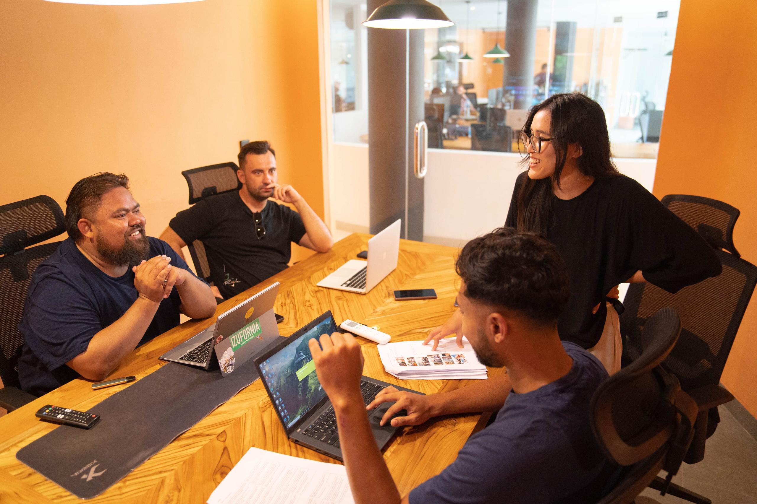 Four people collaborating around a table with laptops in a meeting room