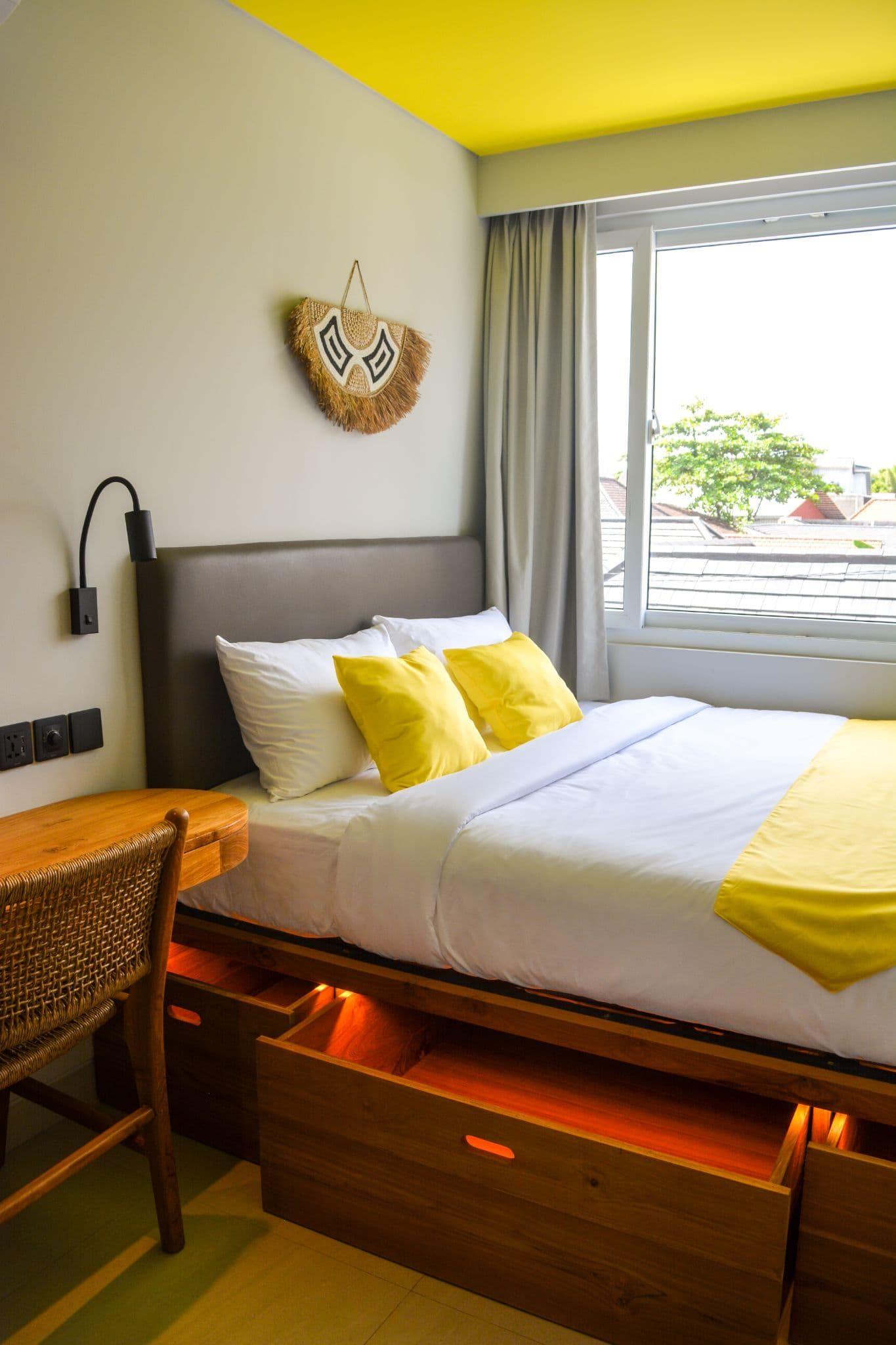 Premium coliving room with double bed, wooden desk, yellow accent pillows and ceiling, and window with garden view