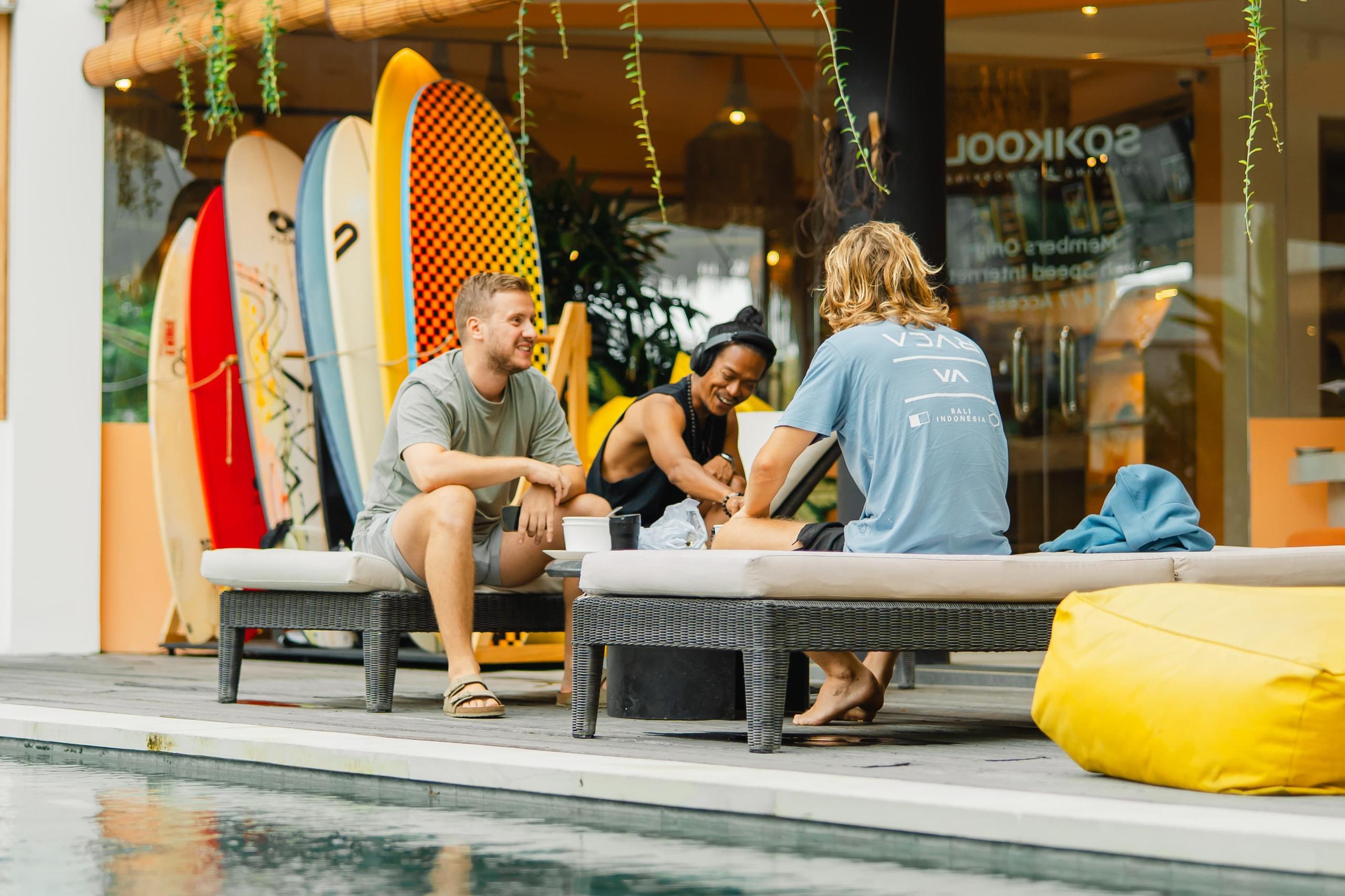 Three residents socializing by the swimming pool with surfboards in the background and the Sokkool sign visible