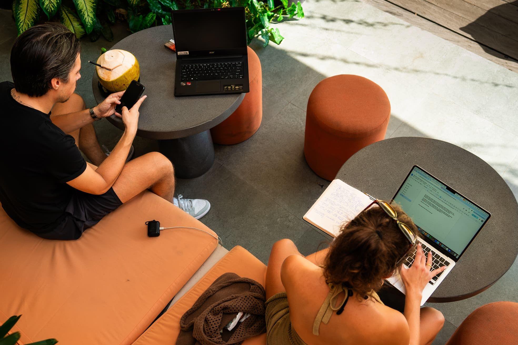 Two residents working on laptops in the outdoor lounge area with terracotta-colored furniture