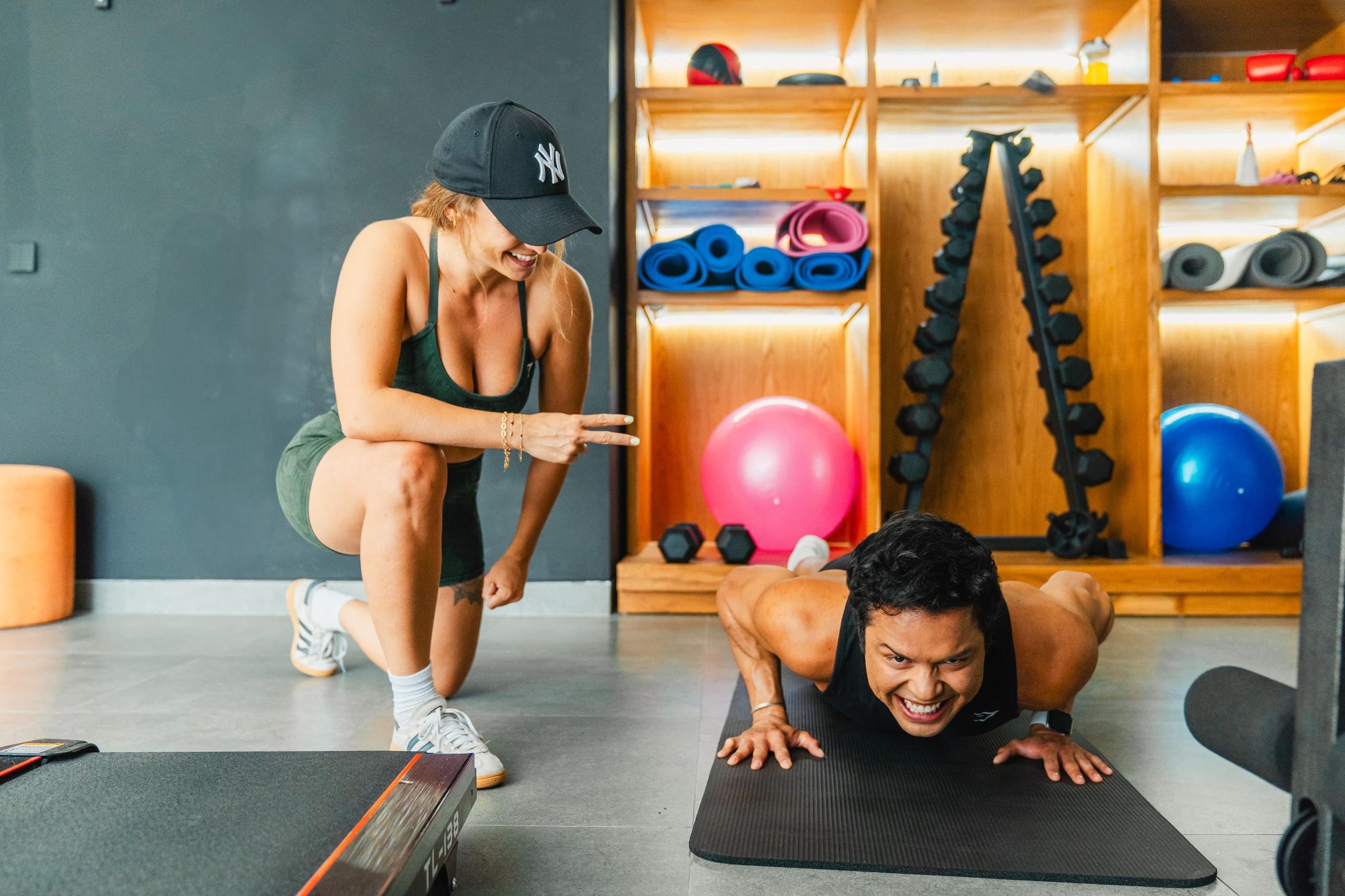 Two people exercising in the gym — one doing push-ups while the other coaches