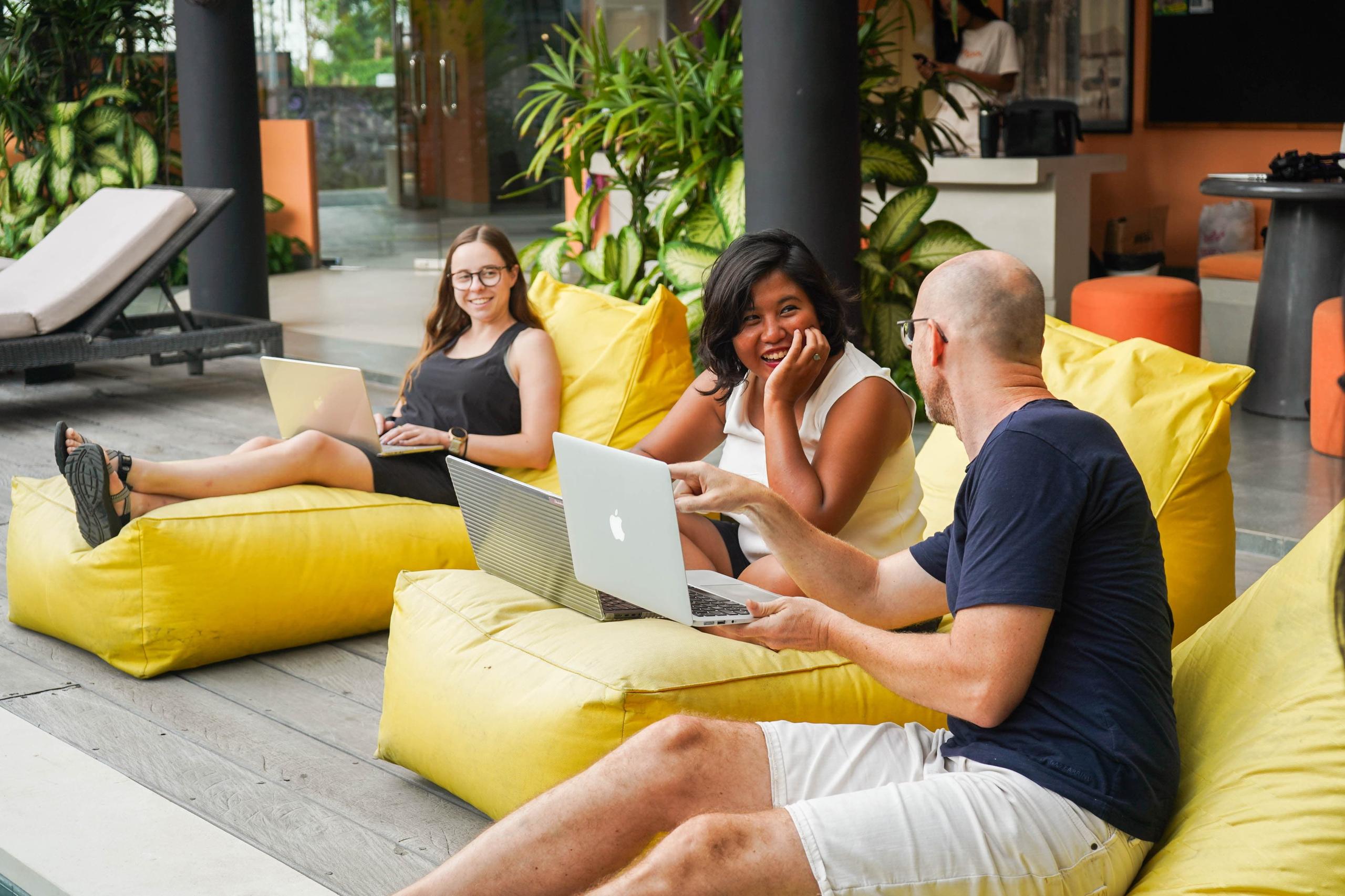 Three members working on laptops while relaxing on yellow bean bags in the outdoor area