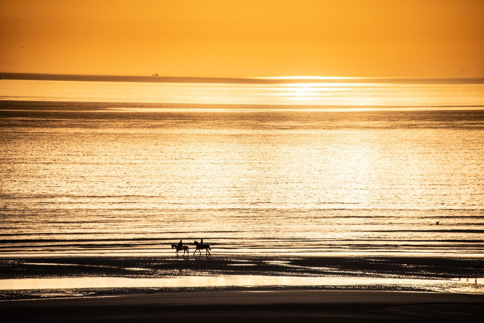 Two horse riders silhouetted on Blackpool beach at golden sunset
