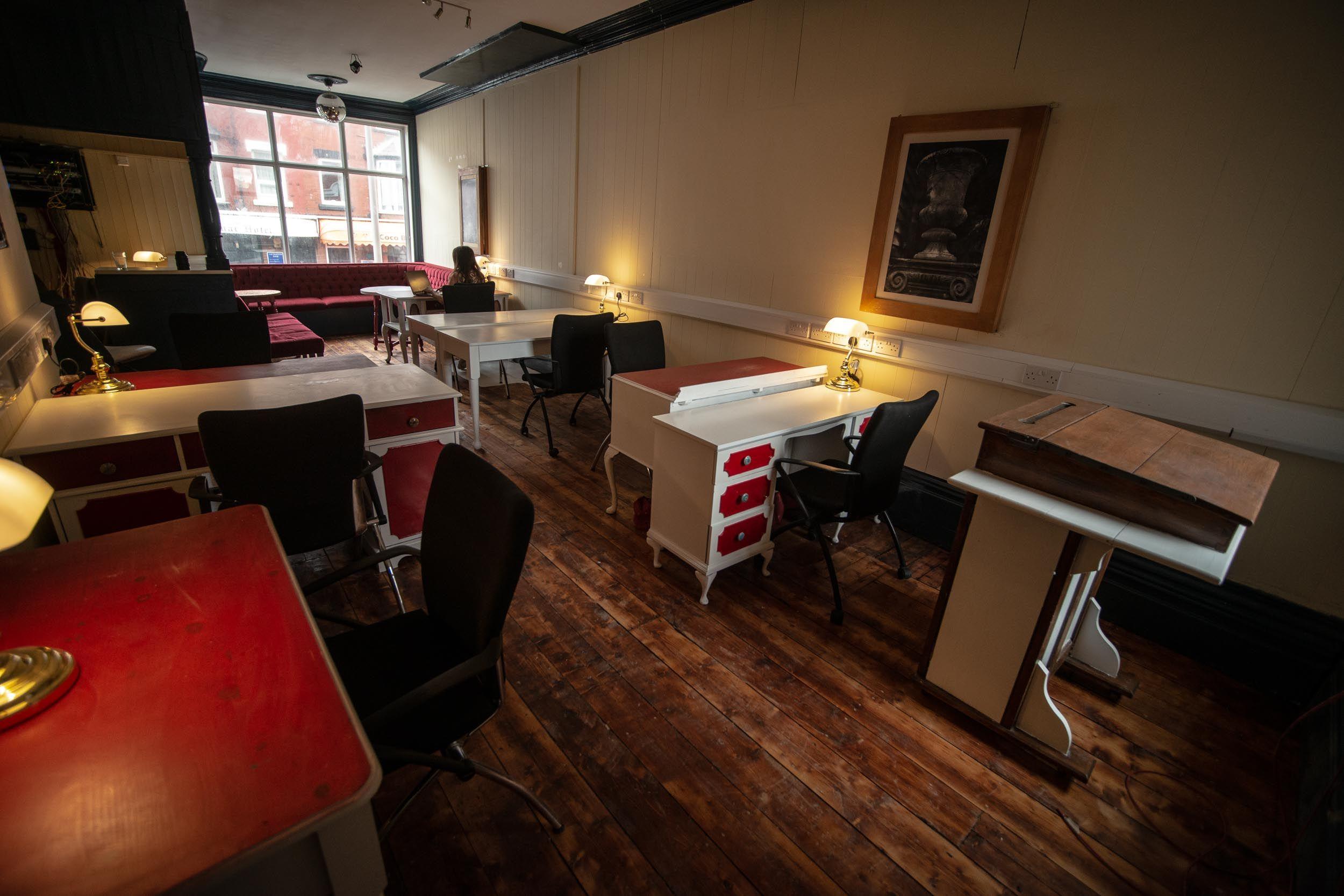 The main coworking room on the ground floor — the original Victorian living room with desks, lamps, and the old bar area in the background