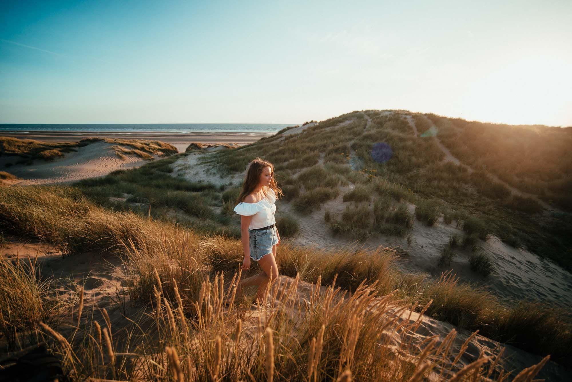 Person standing on sand dunes near Blackpool beach at sunset