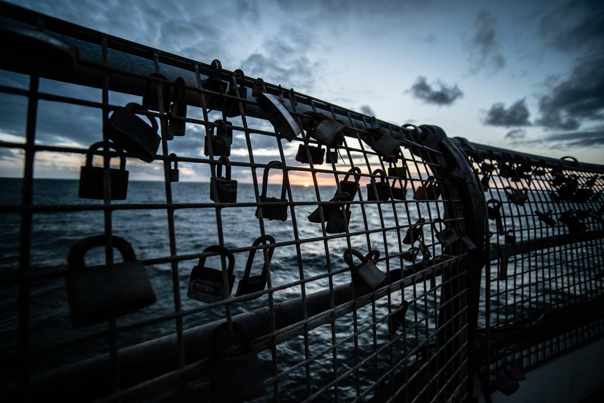 Love locks on a pier railing at sunset with the sea in the background