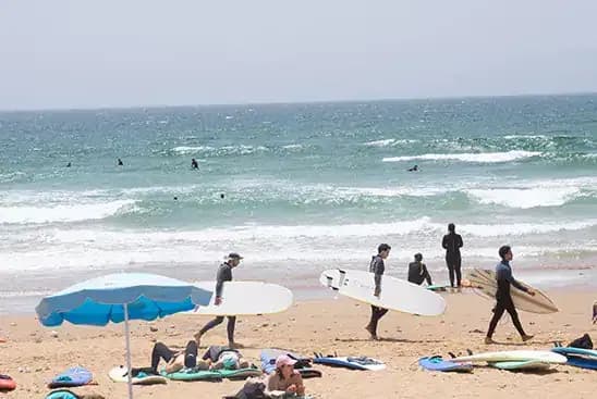 People sunbathing and surfers walking at the beach in Taghazout