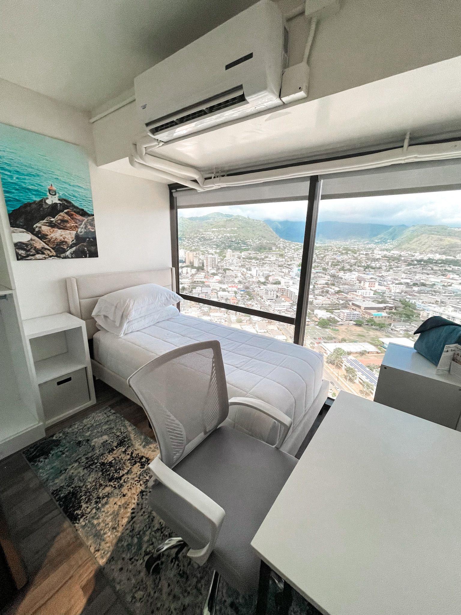 Twin bedroom (Makapu'u room) with single bed, desk, chair, and floor-to-ceiling window with mountain and city views