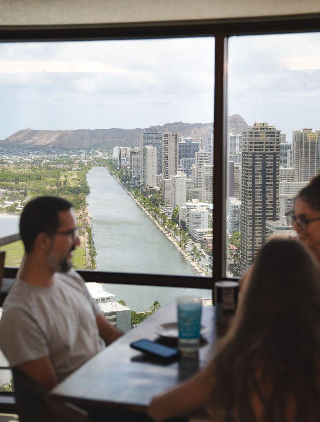 Two members sitting at the dining table with panoramic views of Honolulu, Ala Wai Canal, and Diamond Head through floor-to-ceiling windows