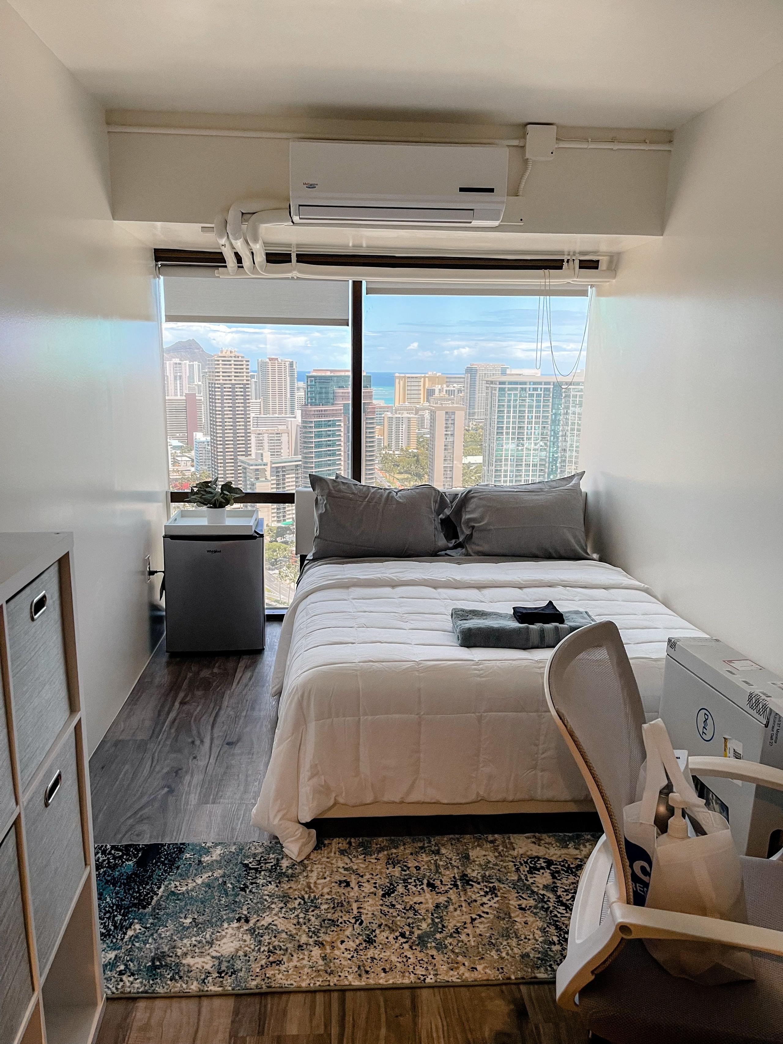 Queen bedroom (Publics room) with double bed, desk, chair, mini-fridge, and floor-to-ceiling window with city and ocean views