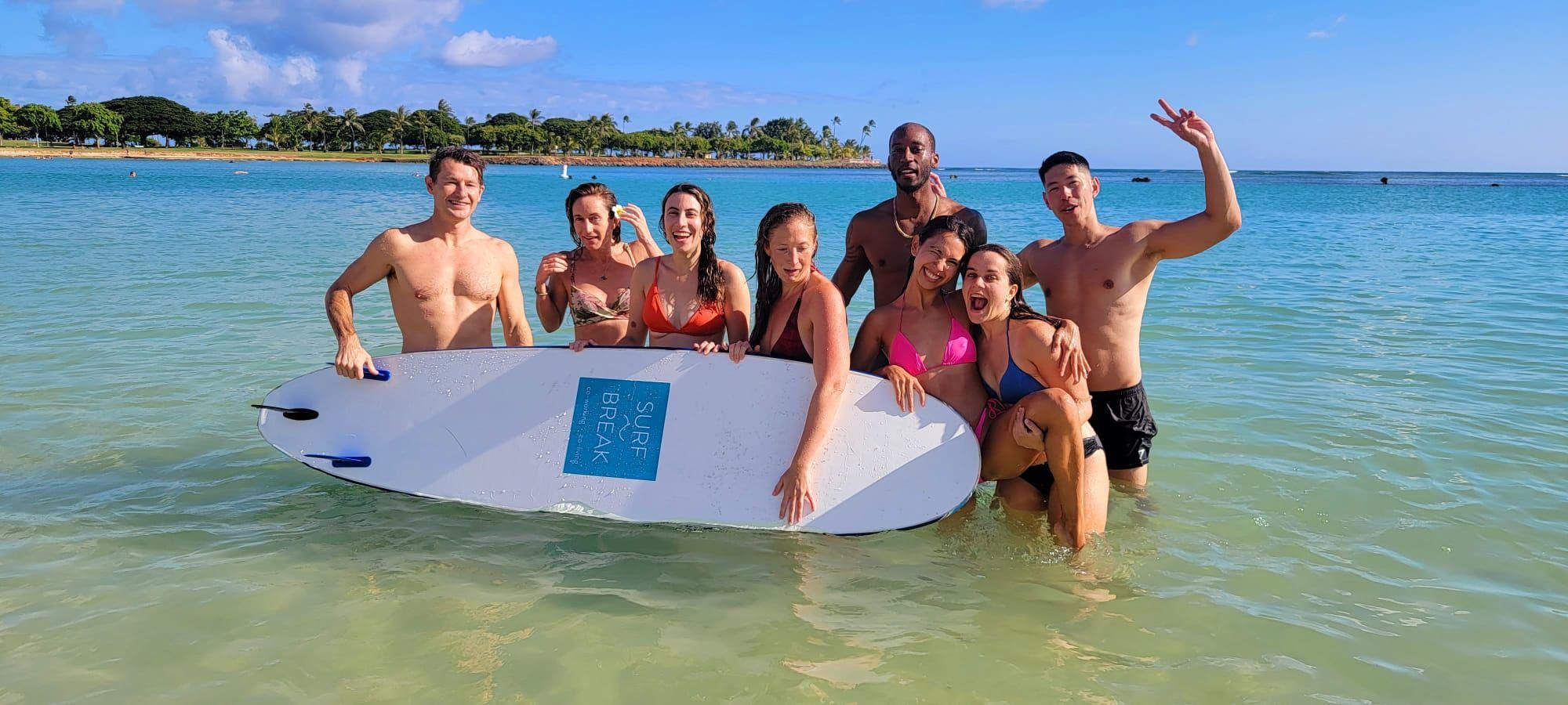 Group of Surfbreak members in the ocean holding a Surfbreak surfboard at a beach in Honolulu