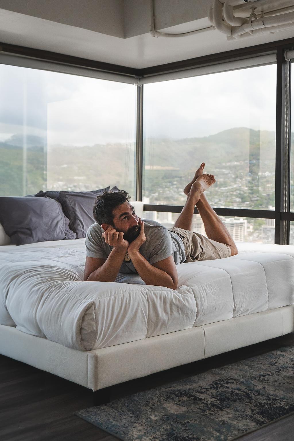 Member relaxing on a king bed in a private room with floor-to-ceiling windows overlooking Honolulu mountains