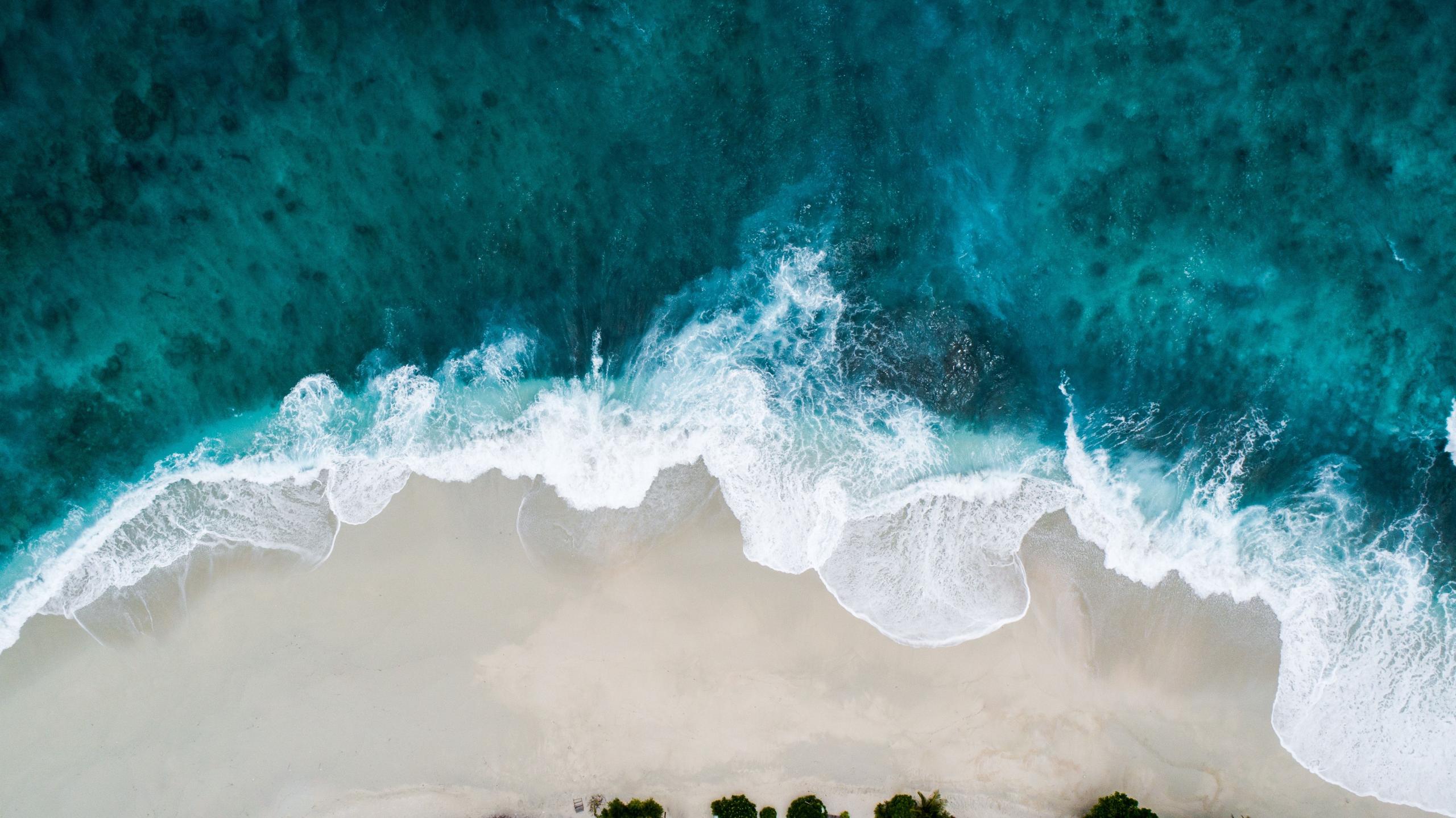 Aerial view of turquoise ocean waves meeting a white sandy beach in Hawaii