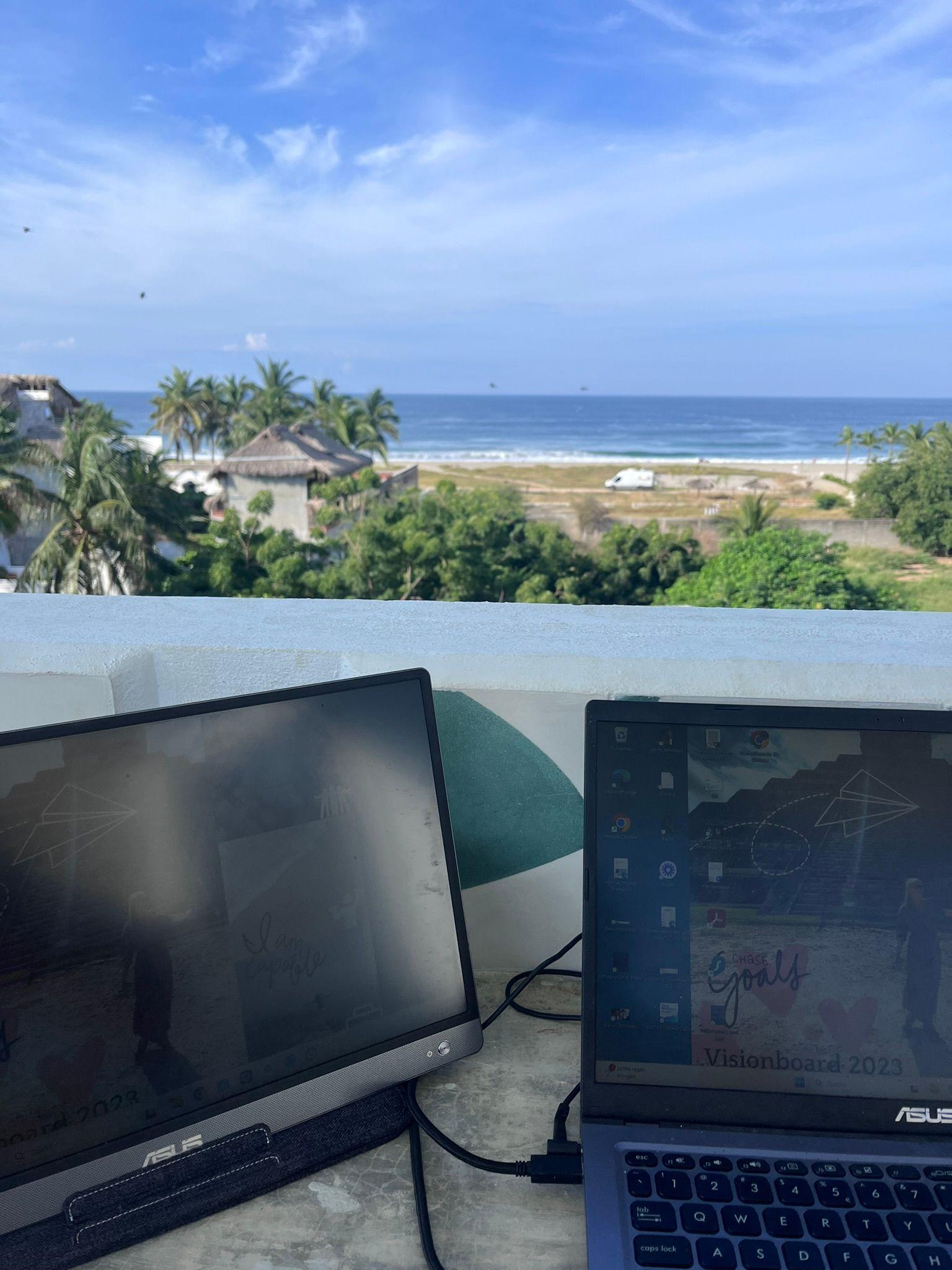 Laptop setup on the shaded rooftop work area at Surfbreak PXM with ocean view in the background