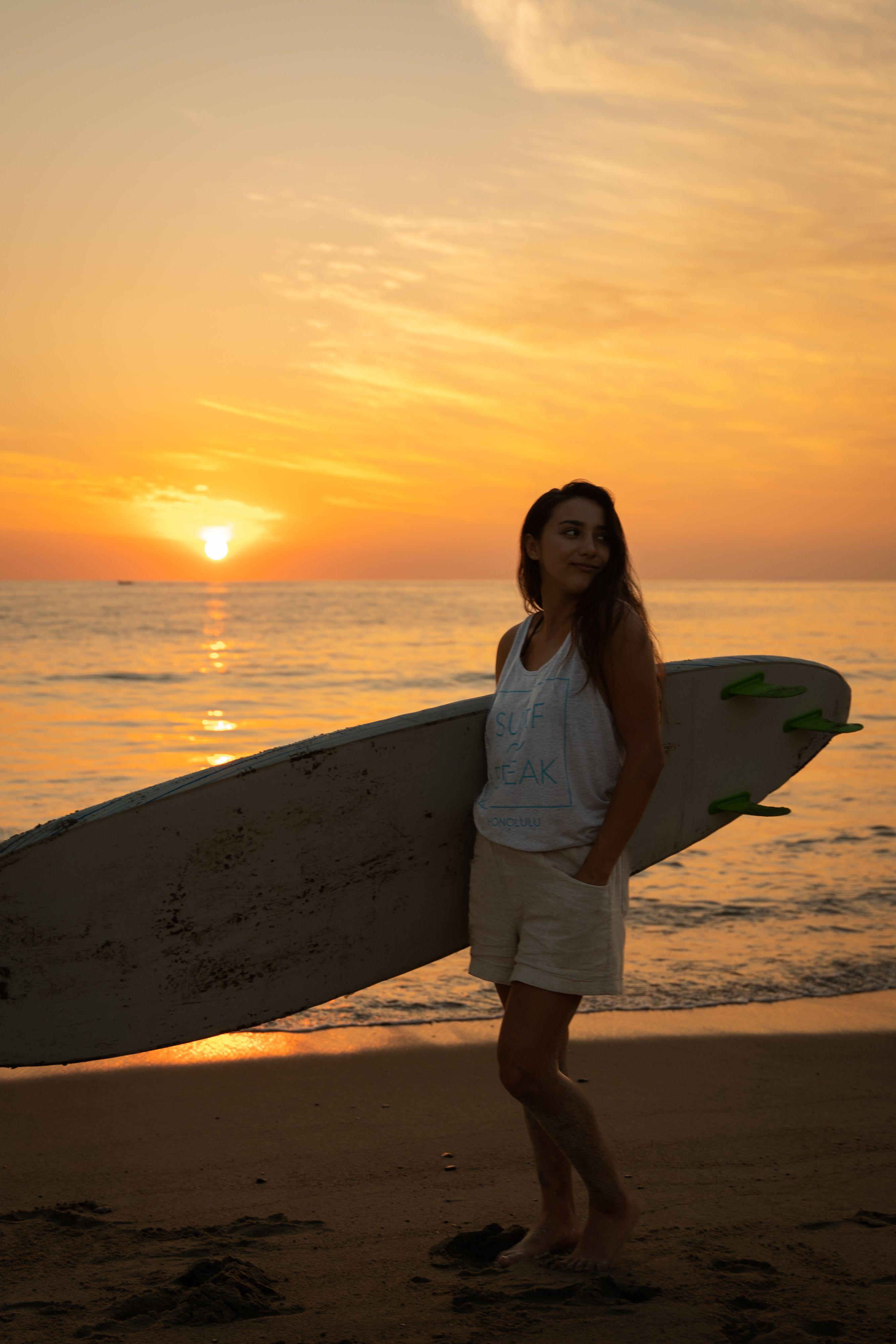 A member carrying a surfboard on the beach at sunset in Puerto Escondido