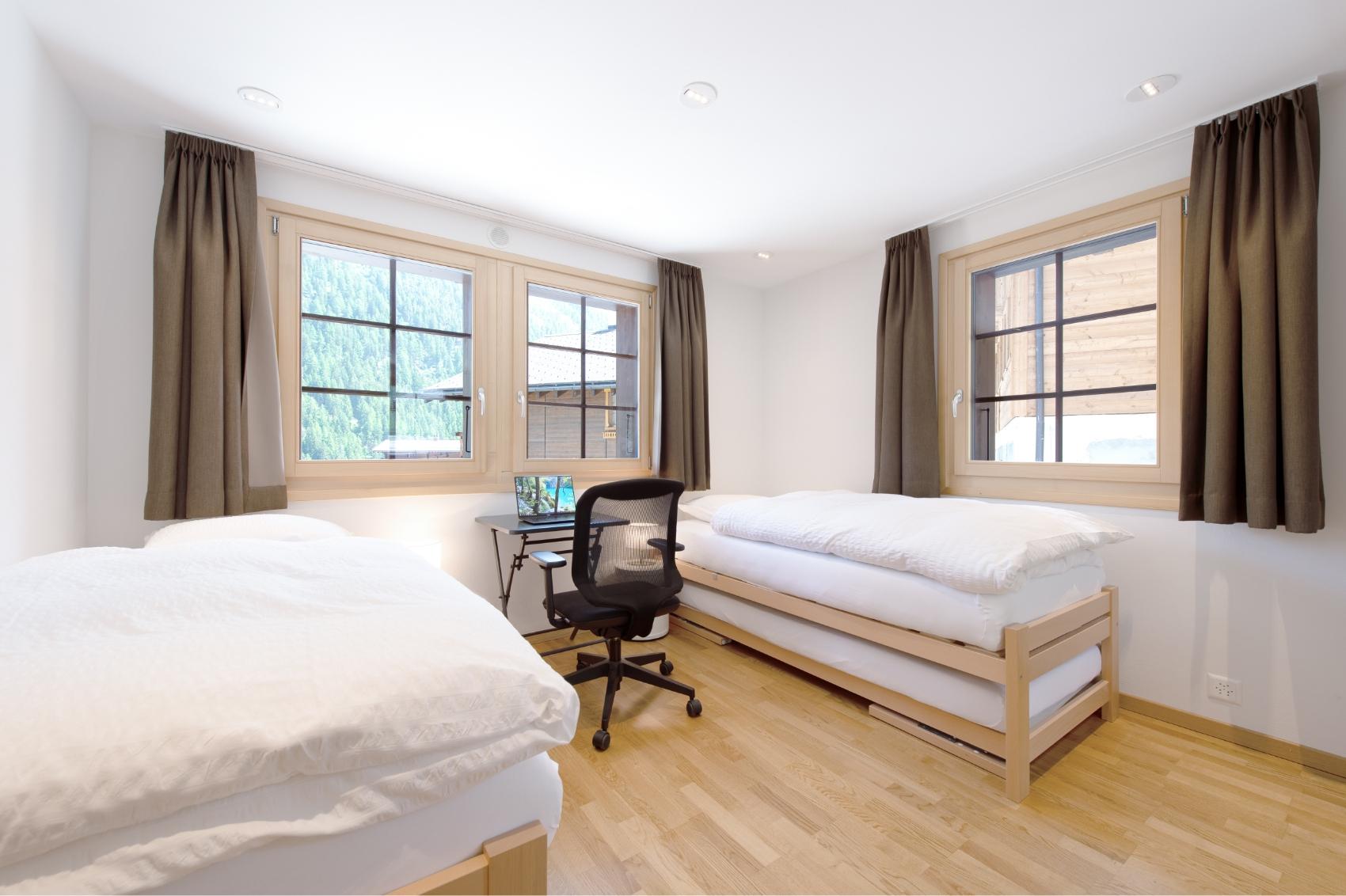 Twin shared room with two single beds, a desk and ergonomic chair, and windows with mountain views