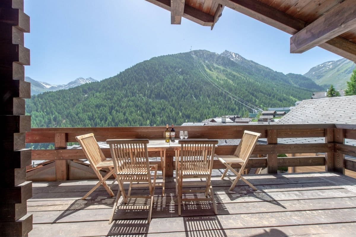Wooden terrace with table and chairs offering a panoramic view of the Alps and ski slopes