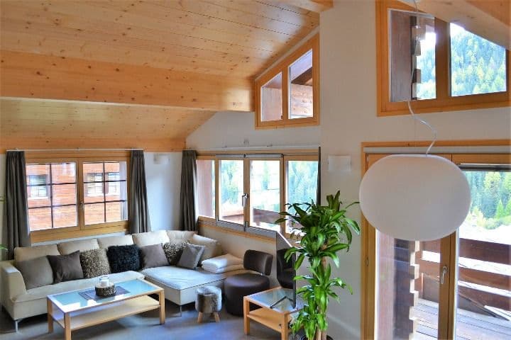 Open lounge area in the Swiss Escape chalet with large sofa, coffee table, and panoramic windows overlooking the forest